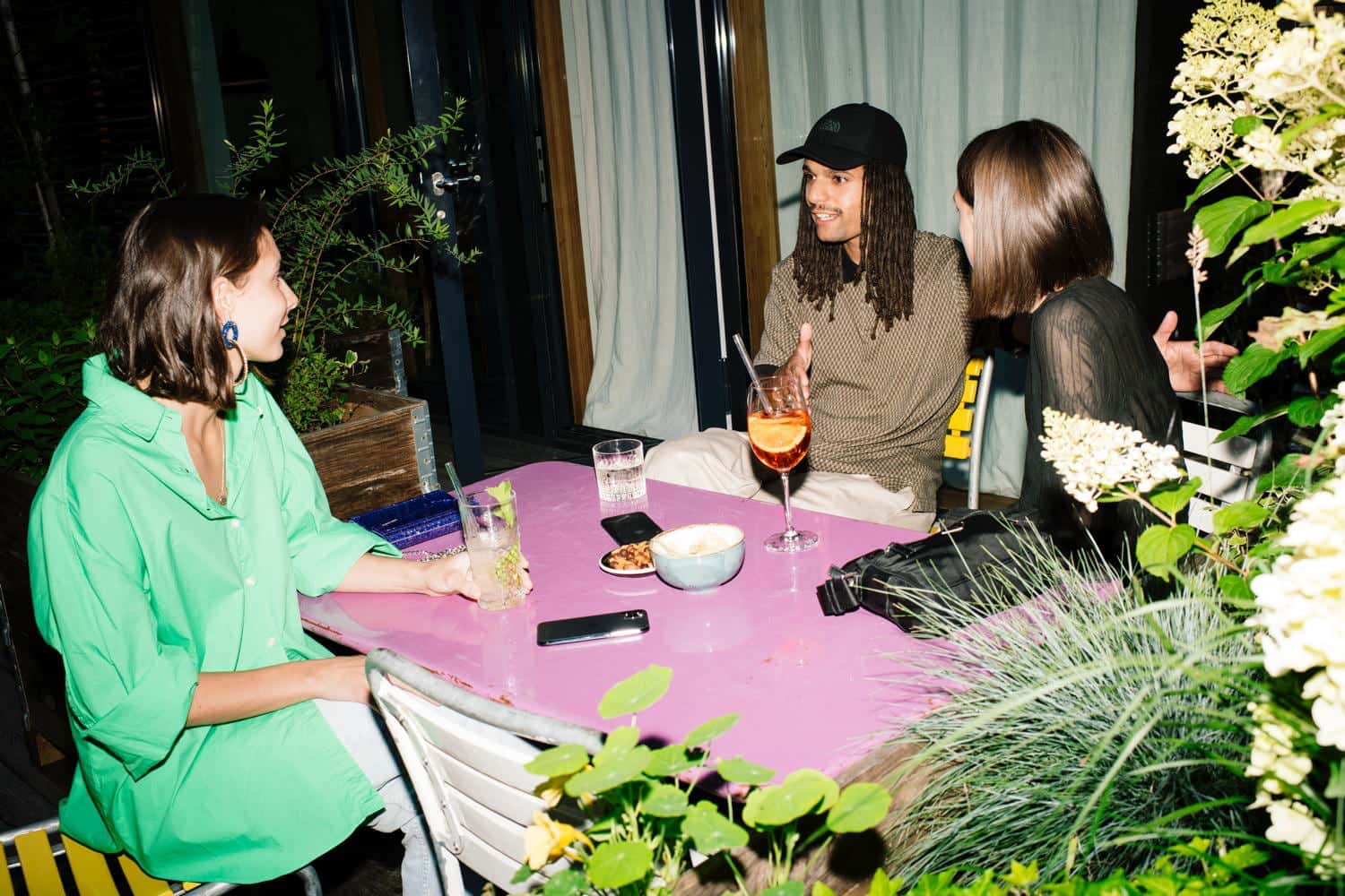 Zwei Frauen und ein Mann sitzen auf an einem Tisch im Aussenbereich des Hotels