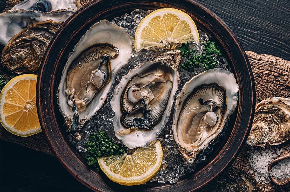 Oysters in a bowl of ice and lemons on a dark wood table top