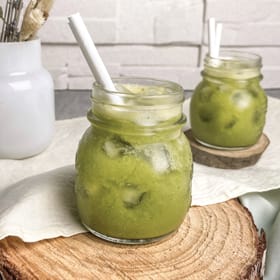 Two small jars of fresh green smoothie and ice cubes. Each jar has a white paper straw.
