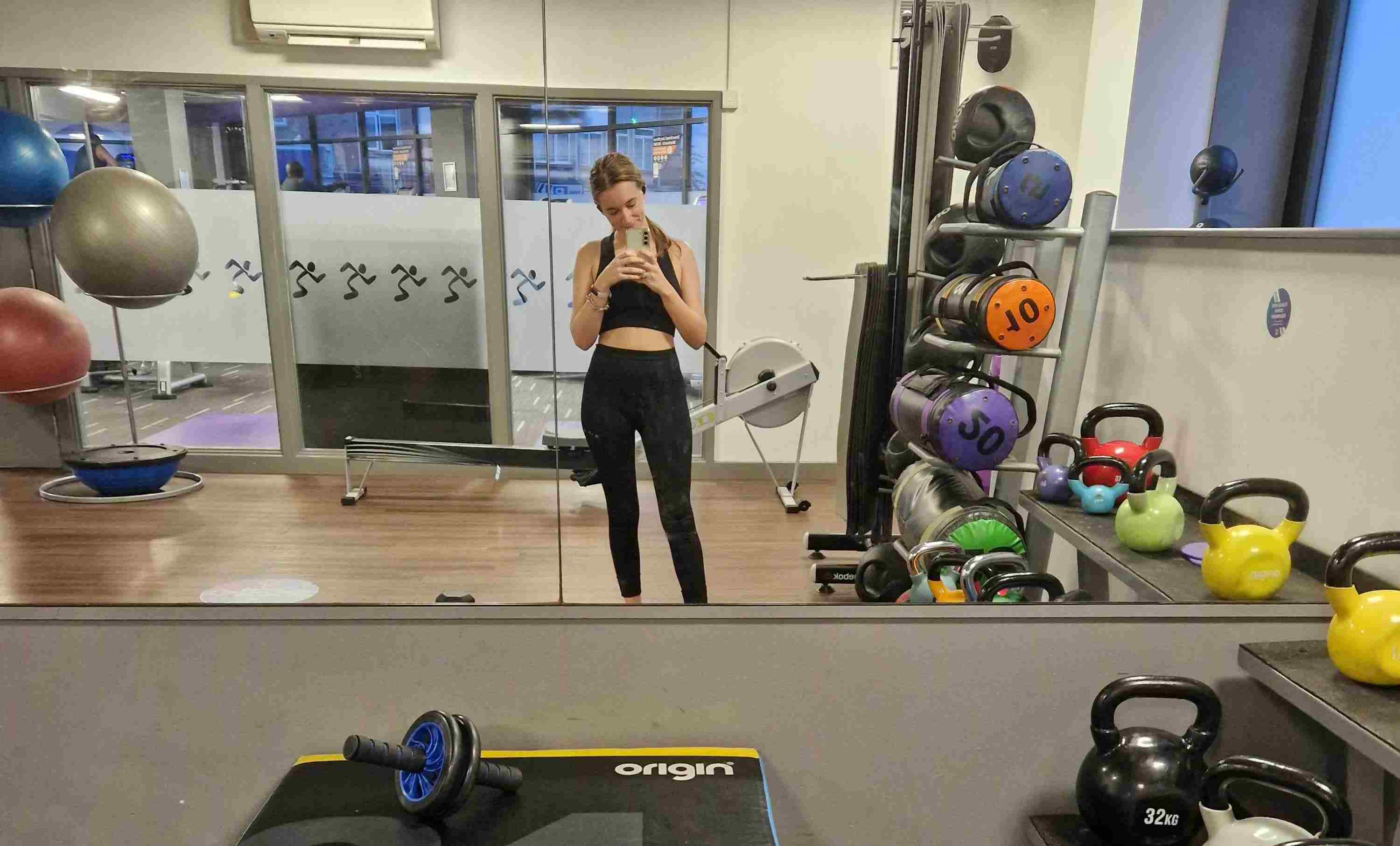 Esther Jade stands in a gym surrounded by weights and exercise balls, with an a roller in the foreground.