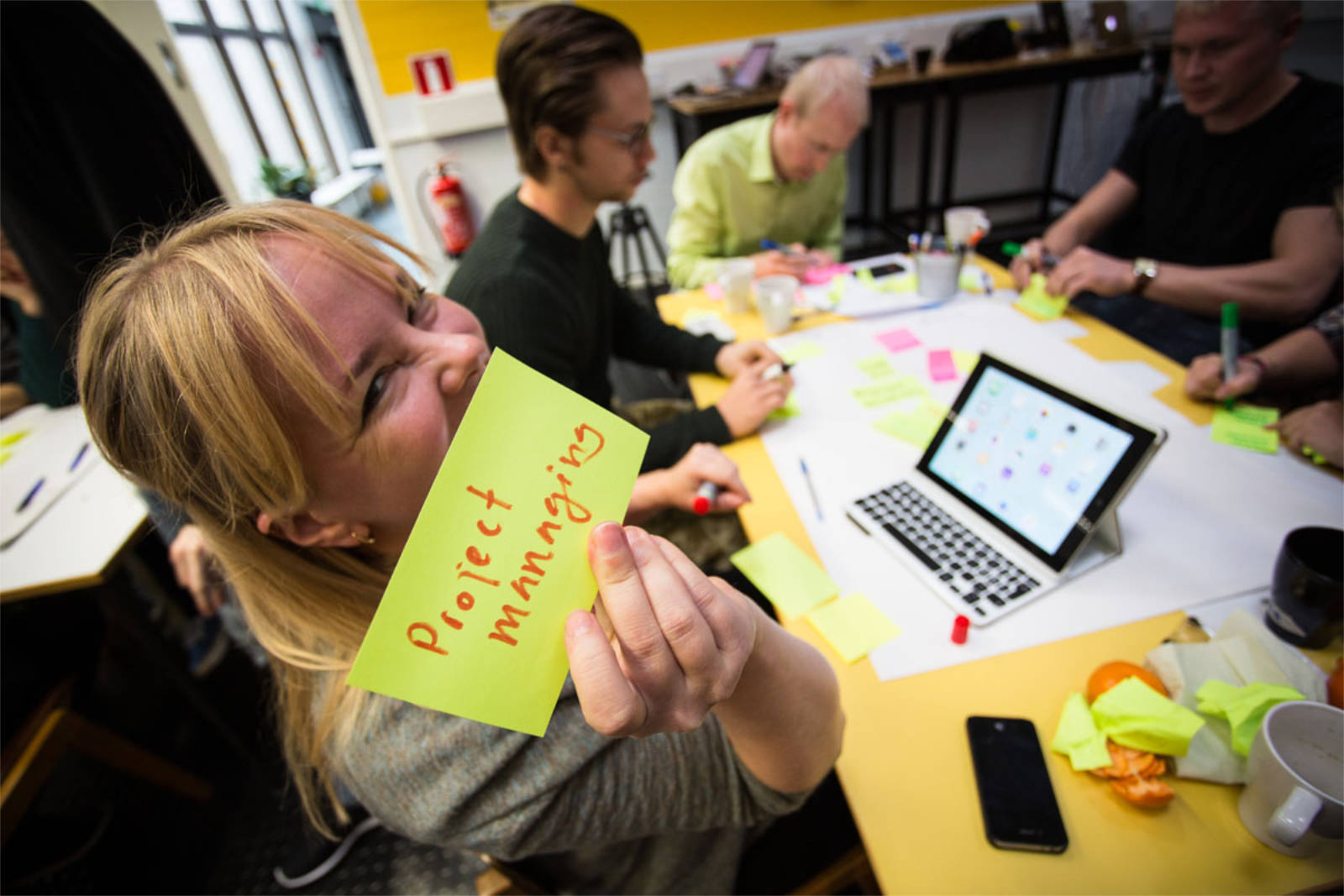 Henkilö näyttää post-it-lappua, jossa lukee "project managing".