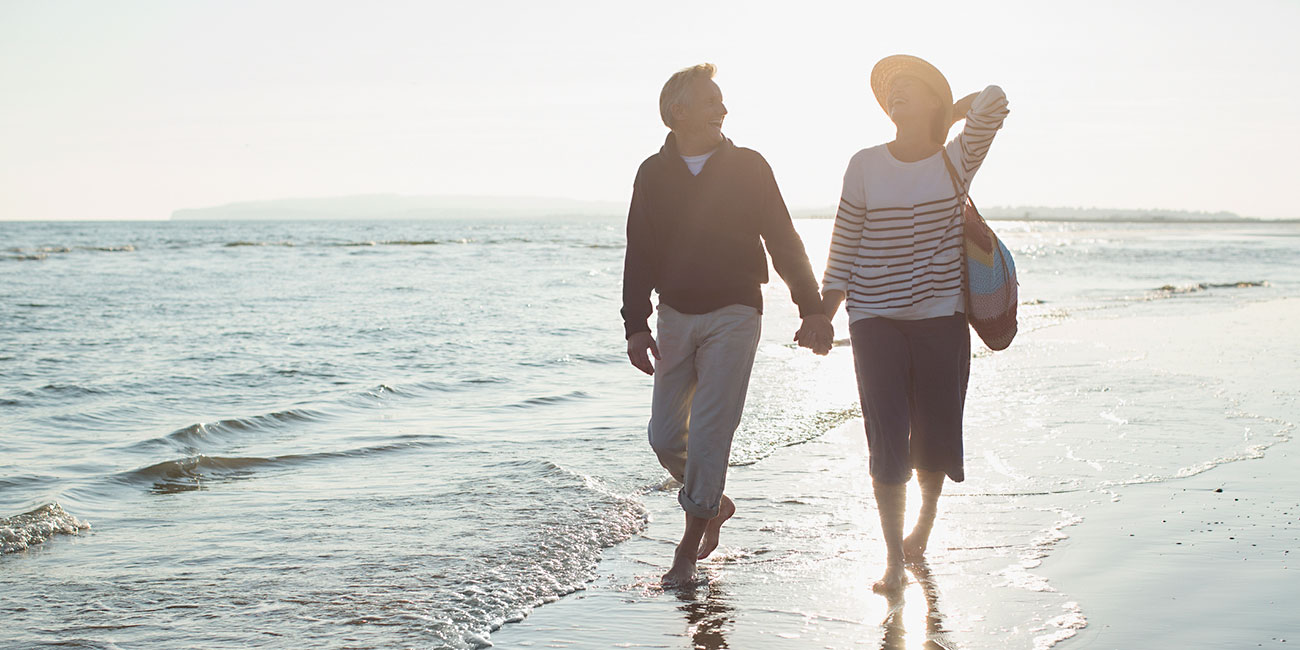Mature couple walking barefoot on sunny beach