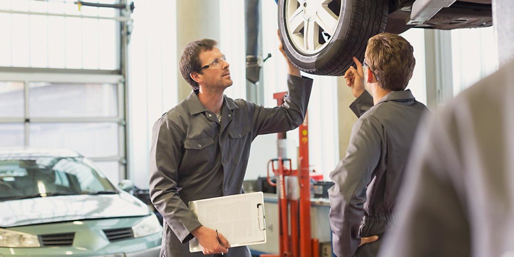 Mechanics examining and discussing tire in auto repair shop