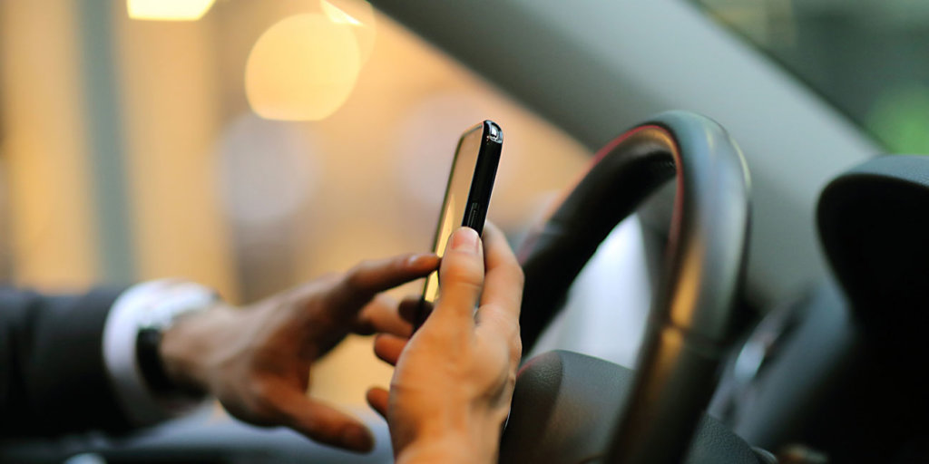 business person texting on his smartphone while driving