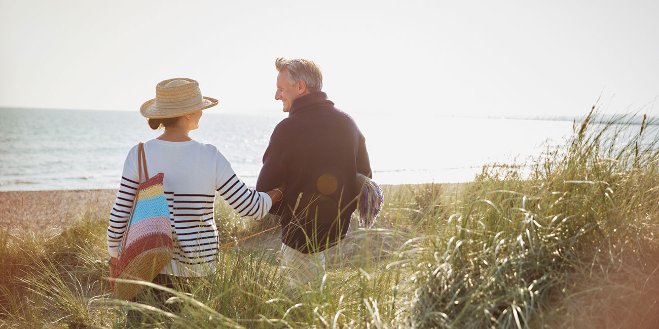 mature couple walking arm in arm in tall grass thinking retirement options