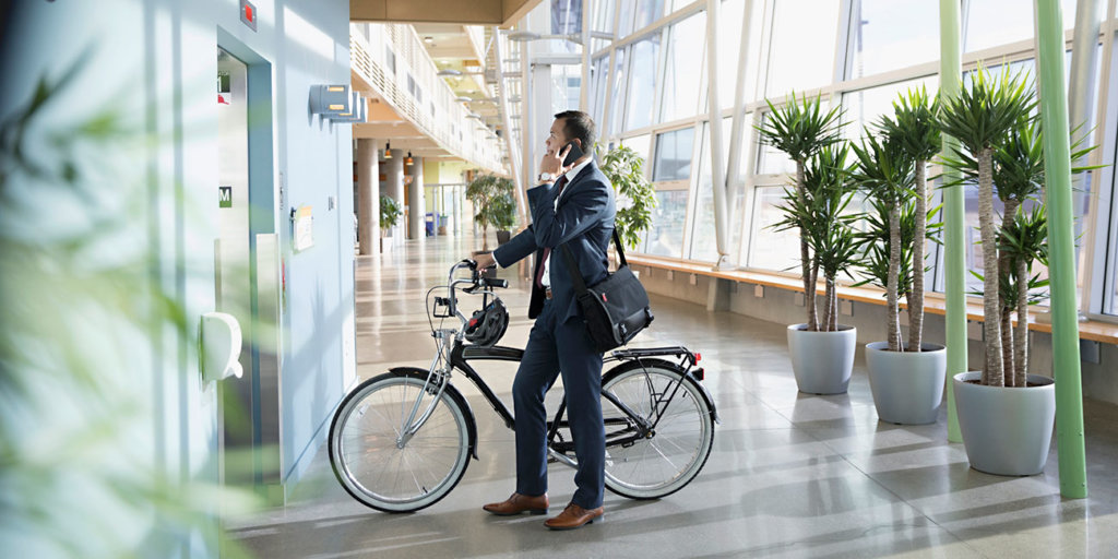 Businessman commuter with bicycle talking on smart phone, waiting at elevator in office lobby
