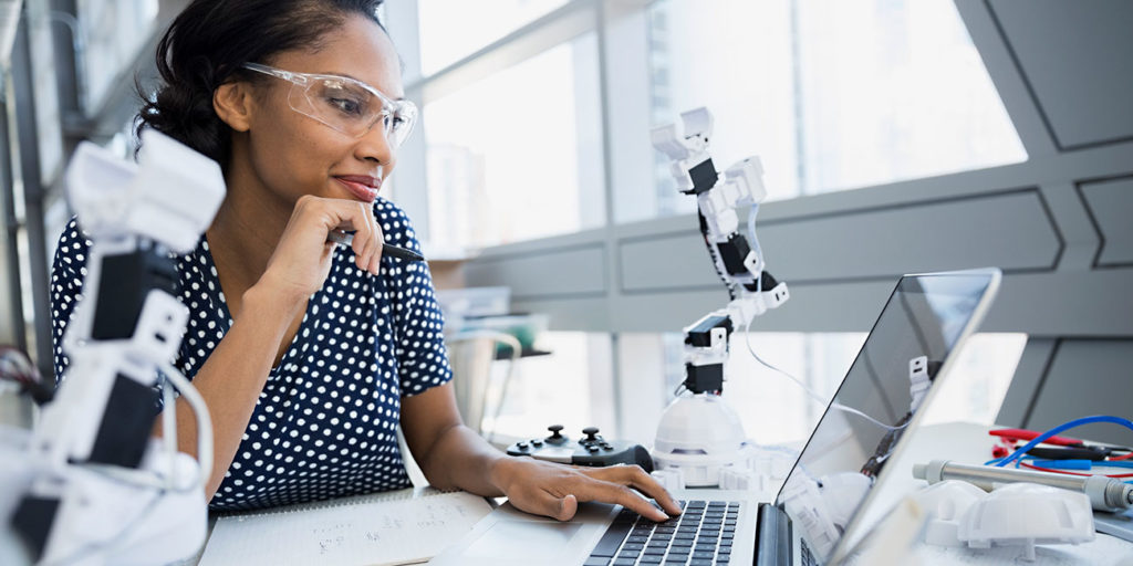 african-american Engineer working at laptop near robotic arms