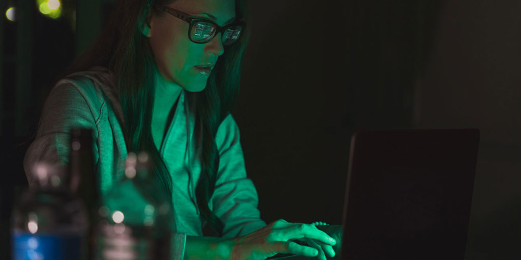 female computer hacker working on a laptop in a dark room