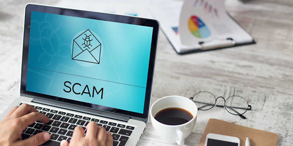 scam concept photo of fingers typing on laptop with scam on screen