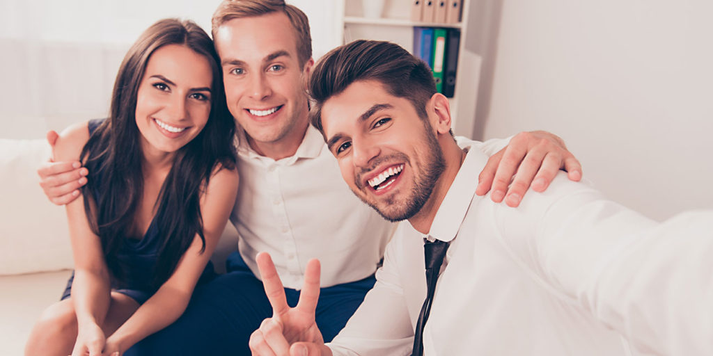 young smiling friends in formalwear take selfie picture on camera