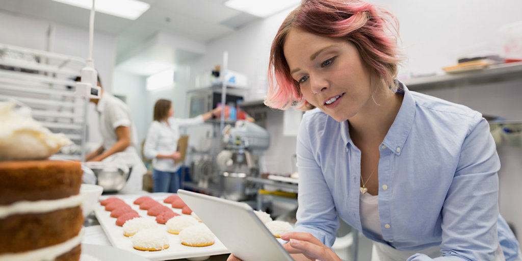 Portrait confident pastry chef working on a digital tablet in a commercial kitchen