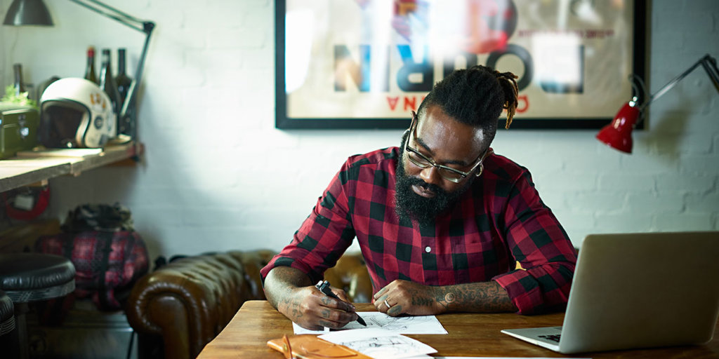 Male designer with tattoos drawing at desk.