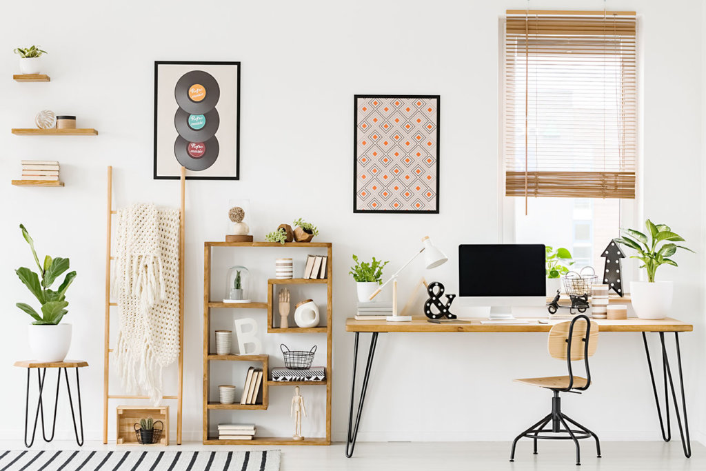 Real photo of a workplace interior with a computer on a desk next to a chair and a shelf with ornaments, posters on a wall and a window with blinds