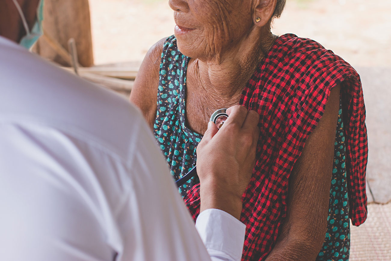 male doctor listening to heart beat of elderly woman in remote area