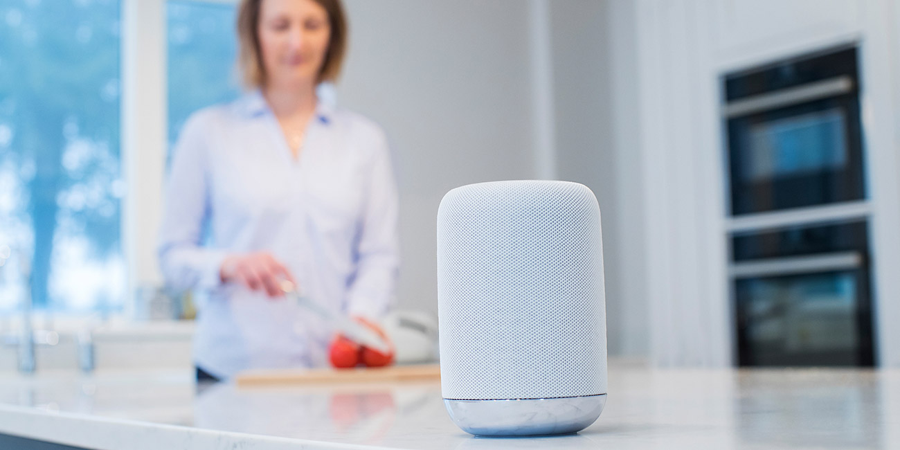 Woman Working In Kitchen With Smart Speaker In Foreground