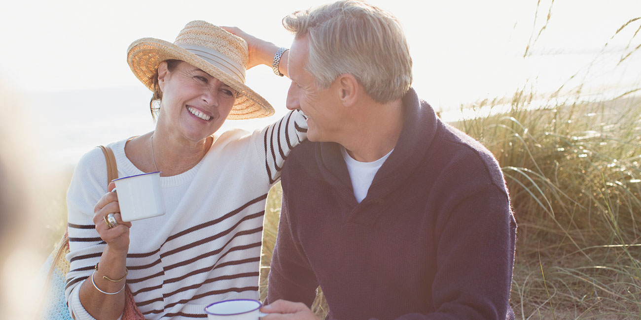 mature couple drinking coffee on sunny beach and grass