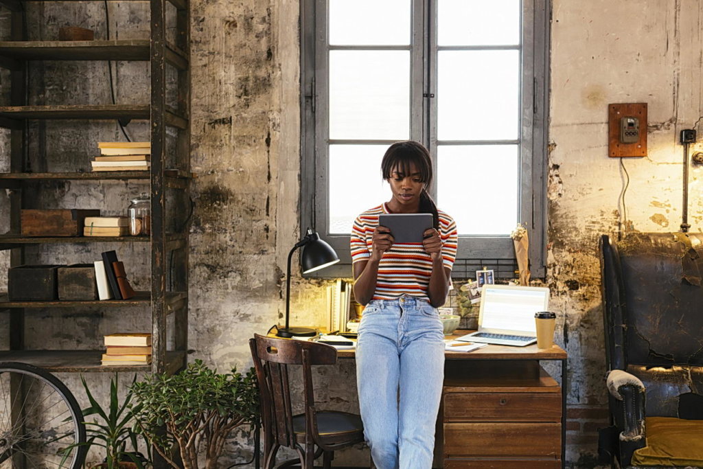 Young woman standing in front of desk in home office using tablet