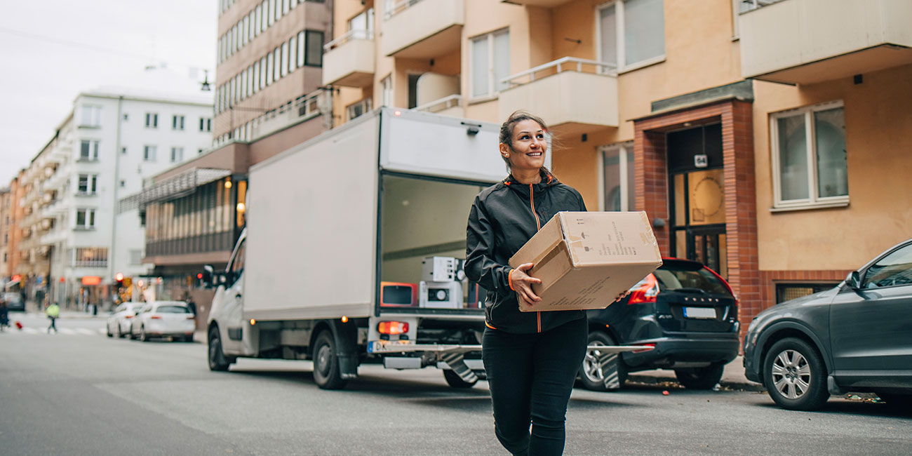 Smiling female messenger carrying box while walking in city
