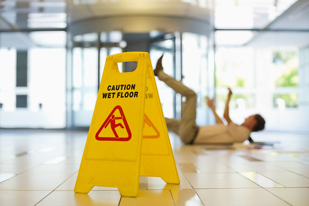 Businessman slipping on wet office floor, caution wet floor sign in foreground