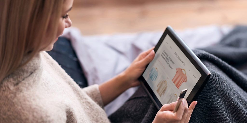 Joyful woman enjoying online shopping in bed