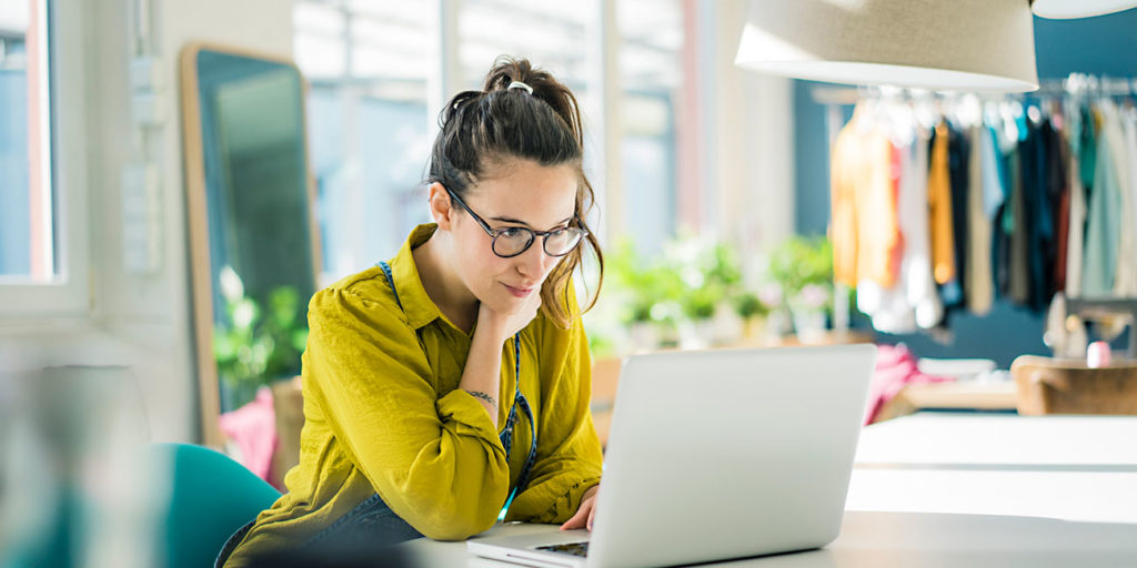 Portrait of smiling fashion designer sitting in her studio using laptop