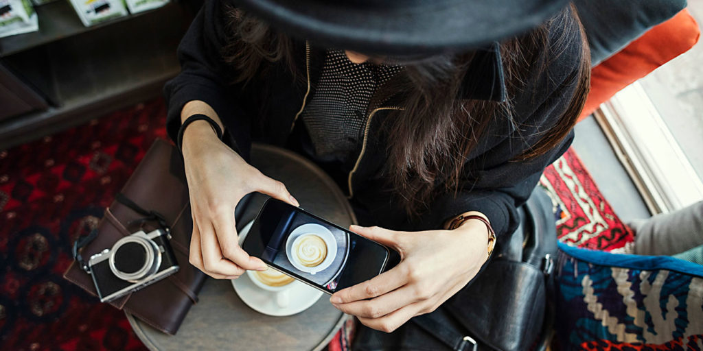 Directly above shot of young woman photographing coffee through smart phone in creative office