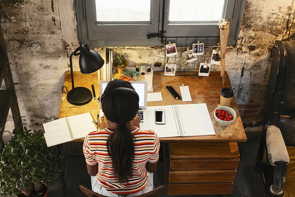 Back view of young woman sitting at desk in home office working on laptop seen from above