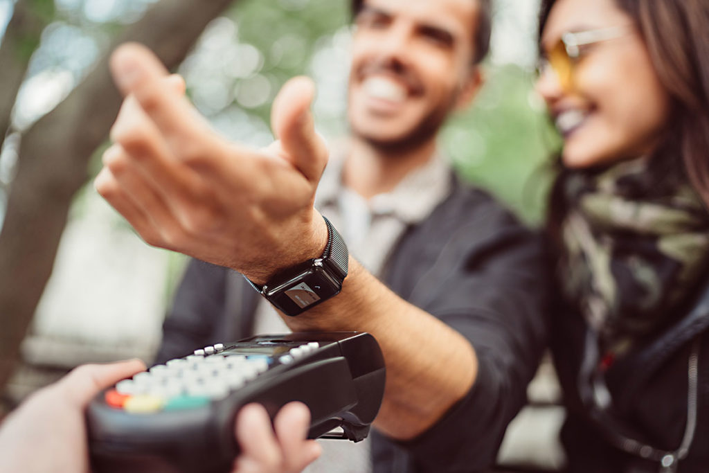 Young man with girlfriend sitting at sidewalk cafe and paying contactless using smartwatch