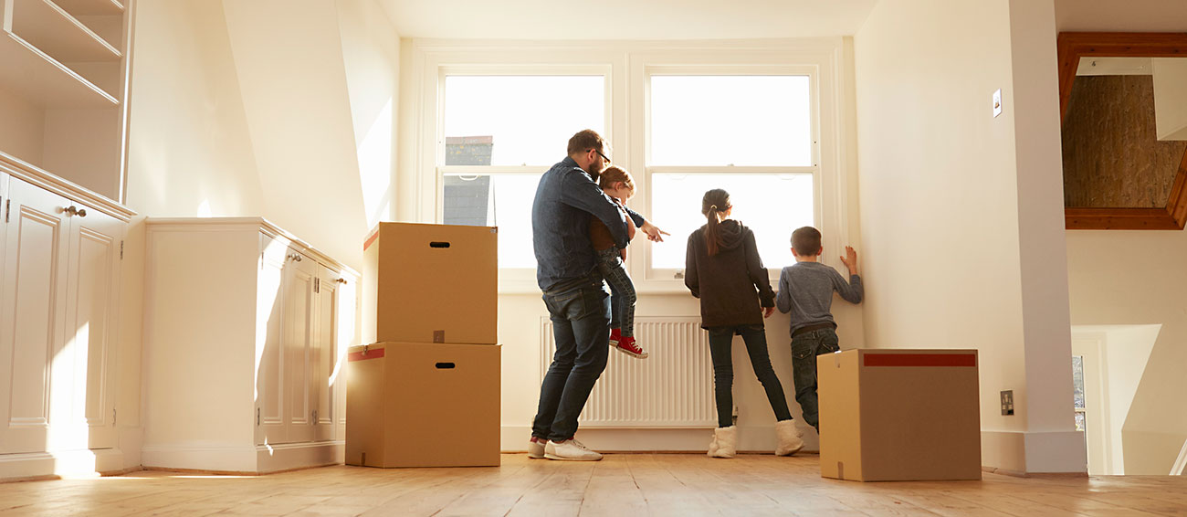 adult man and three children looking from window of new home