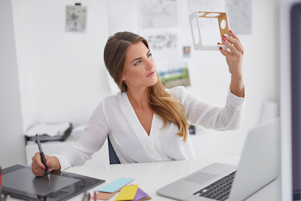 Young woman at desk in office holding model and using graphics tablet