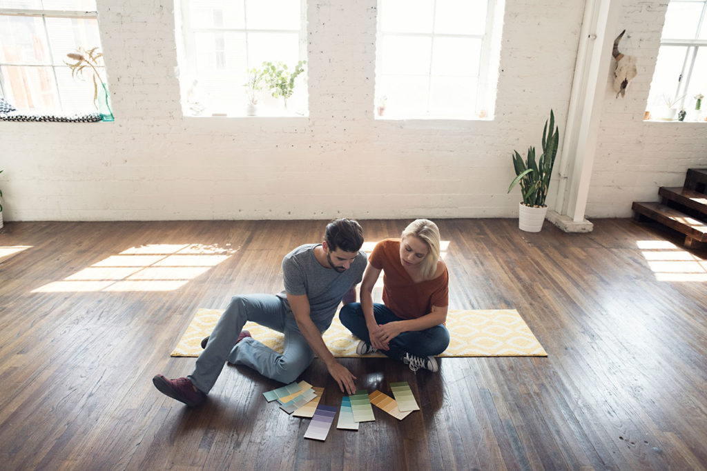 Young homeowners sitting on carpet in a loft looking at color samples