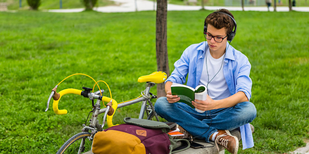 Portrait of male college student with road bicycle sitting on a bench reading a book