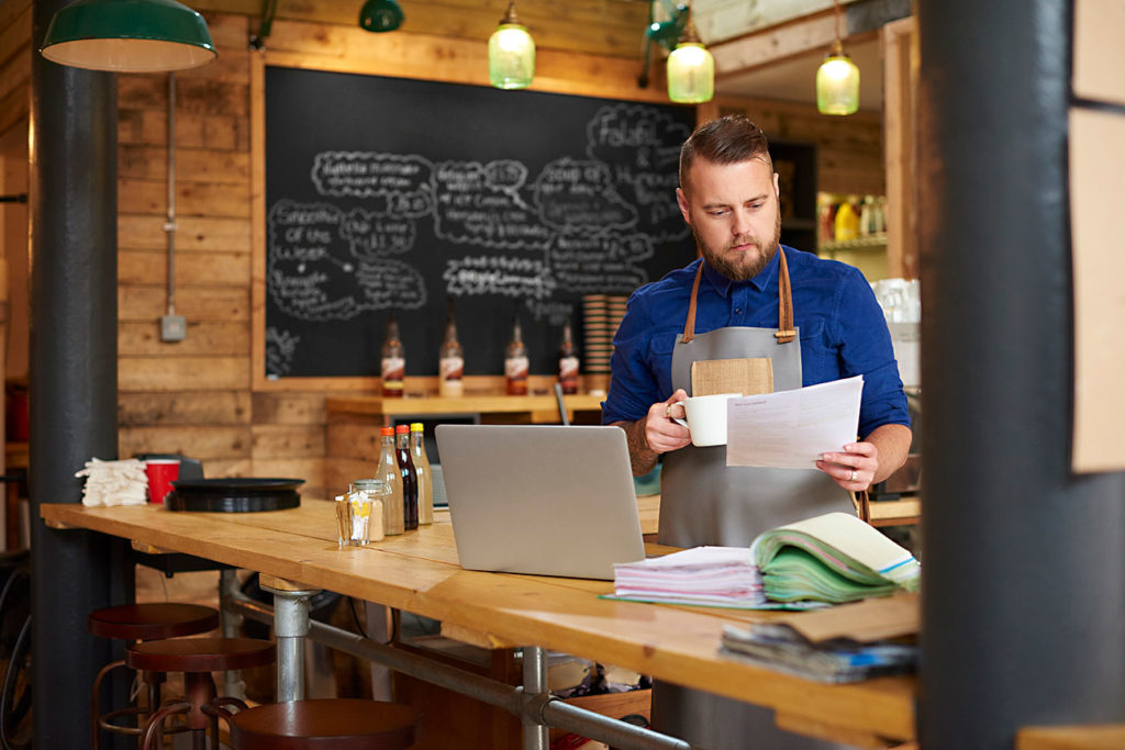 coffee shop owner checks his bookkeeping folder on the counter of his busy coffee shop