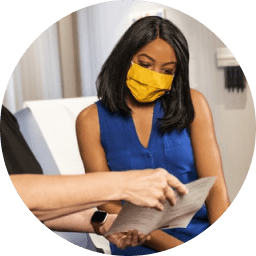 woman sitting on chair looking at Conpago app on tablet with yellow face mask on 