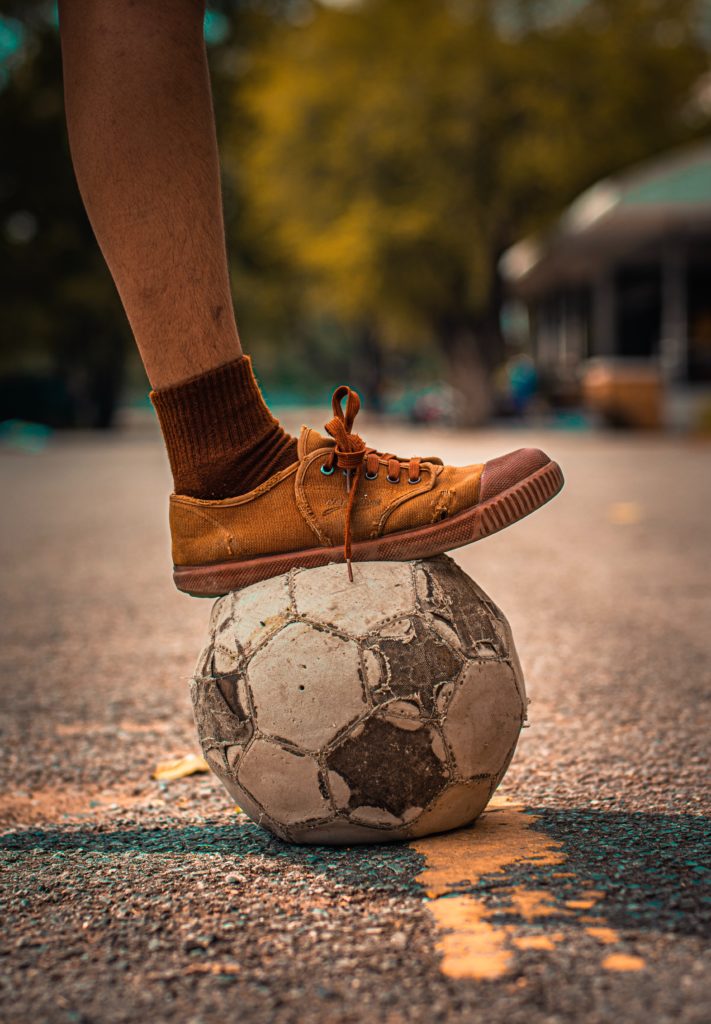 Pieds d'un enfant sur un ballon de foot abimé