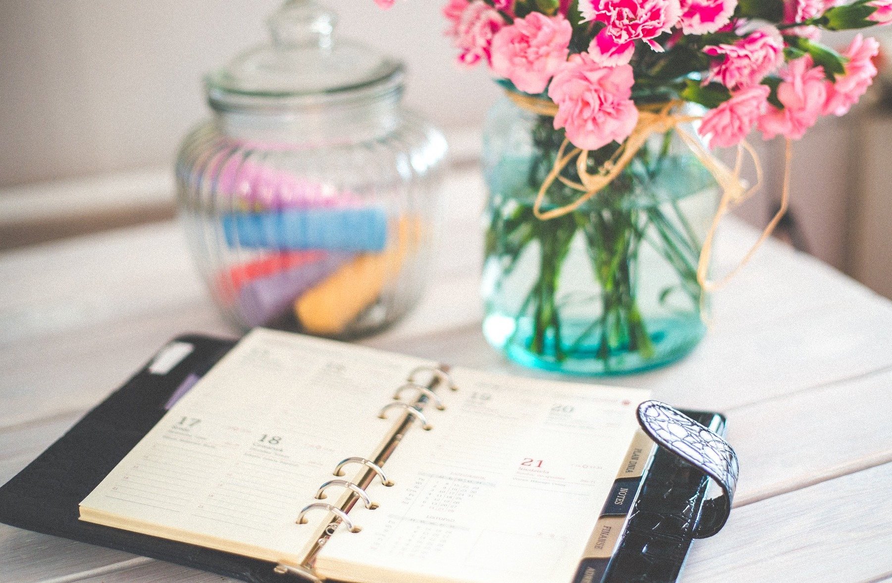 Calendrier sous forme d'agenda posé sur une table avec un pot à crayons et un vase fleuri.