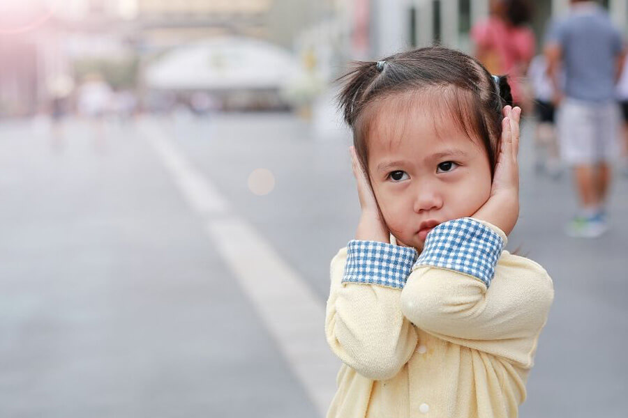 Small girl in city street with hands covering her ears