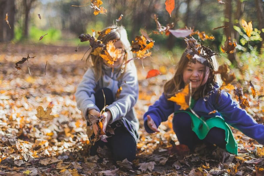 Two small girls playing with autumn leaves on the ground and laughing