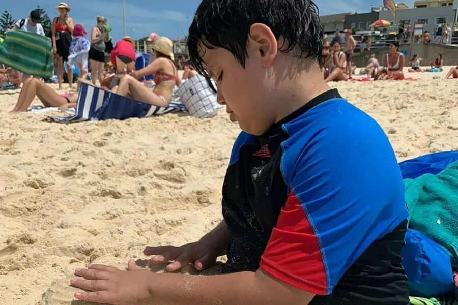 Young boy sitting on beach playing in sand
