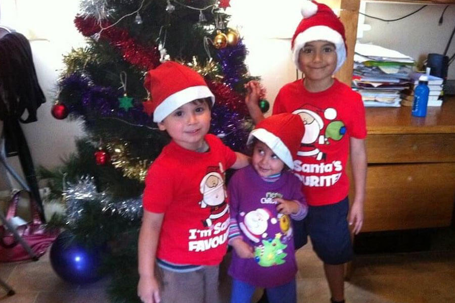 Three young kids wearing Santa hats standing in front of Christmas tree