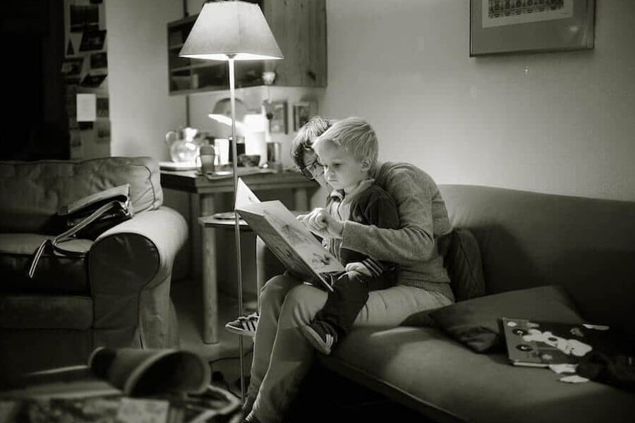 Young boy sitting on his mums lap reading a book
