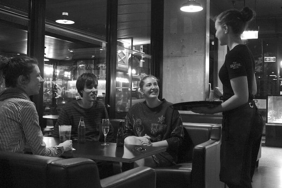 Three young adults in a restaurant ordering meal with waitress