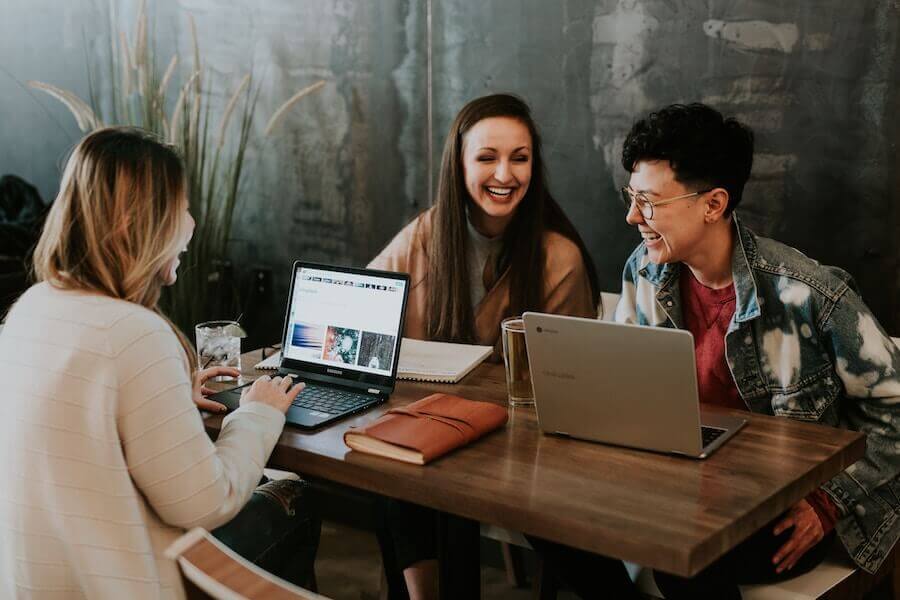 Three young adults on laptops and laughing together
