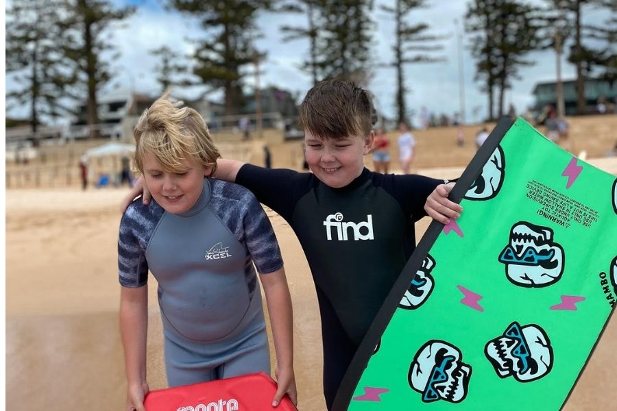 two young autistic boys on beach holding bodyboards