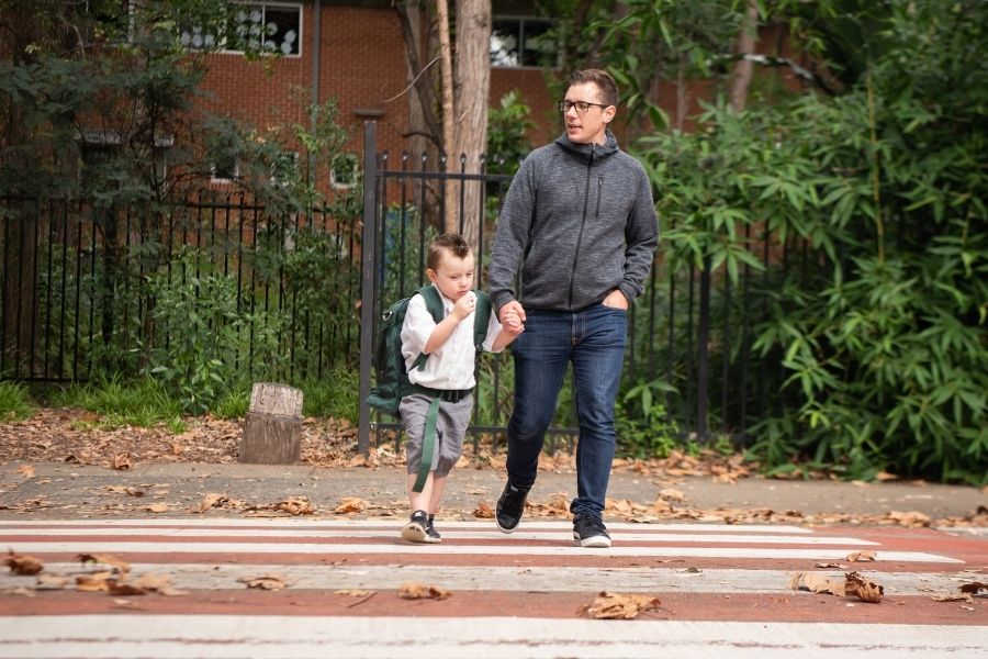 dad and young son walk across a pedestrian crossing to school