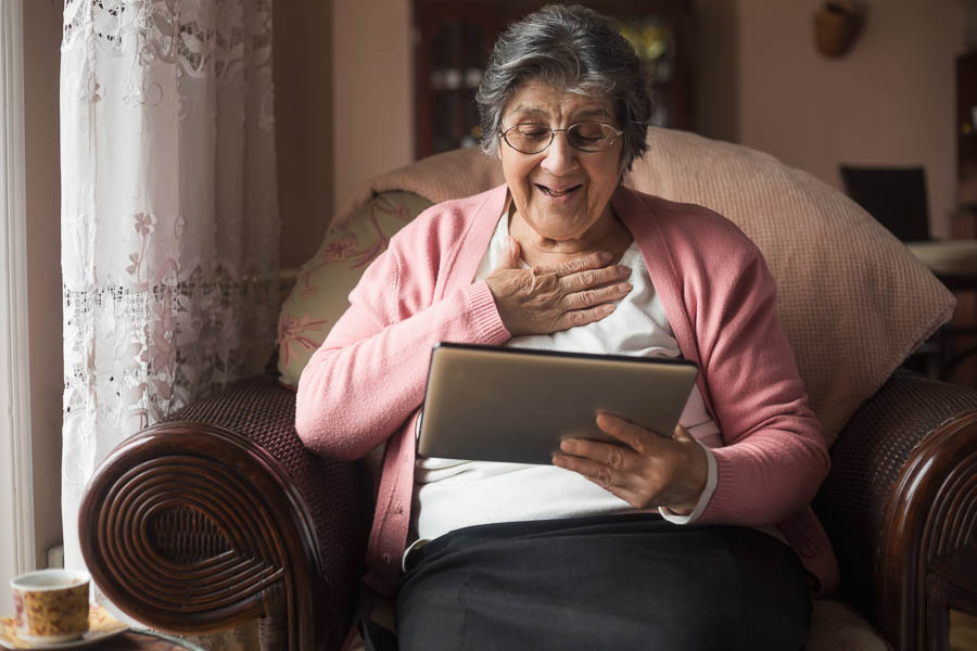 Smiling senior woman using a tablet while holding her hand over her heart.