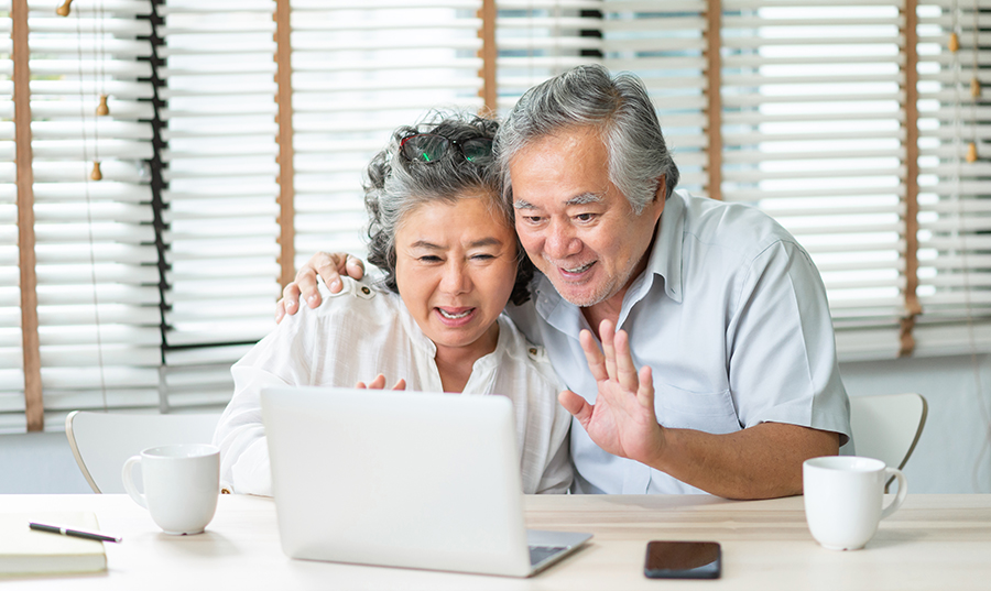 Older couple waving and smiling at computer screen.
