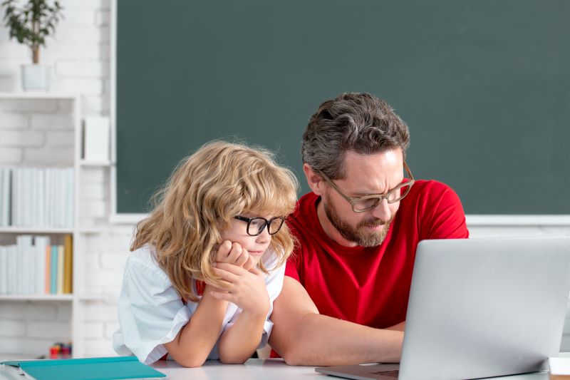 Inteligência Artificial na educação: benefícios e desafios 1 foto de estudante e professor em sala de aula olhando para a tela de notebook com expressão pensativa.