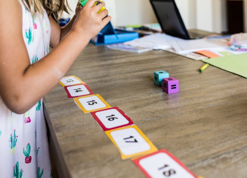 Foto de menina estudante fazendo jogo matemático, com cartões e dados, para se preparar para a obmep.