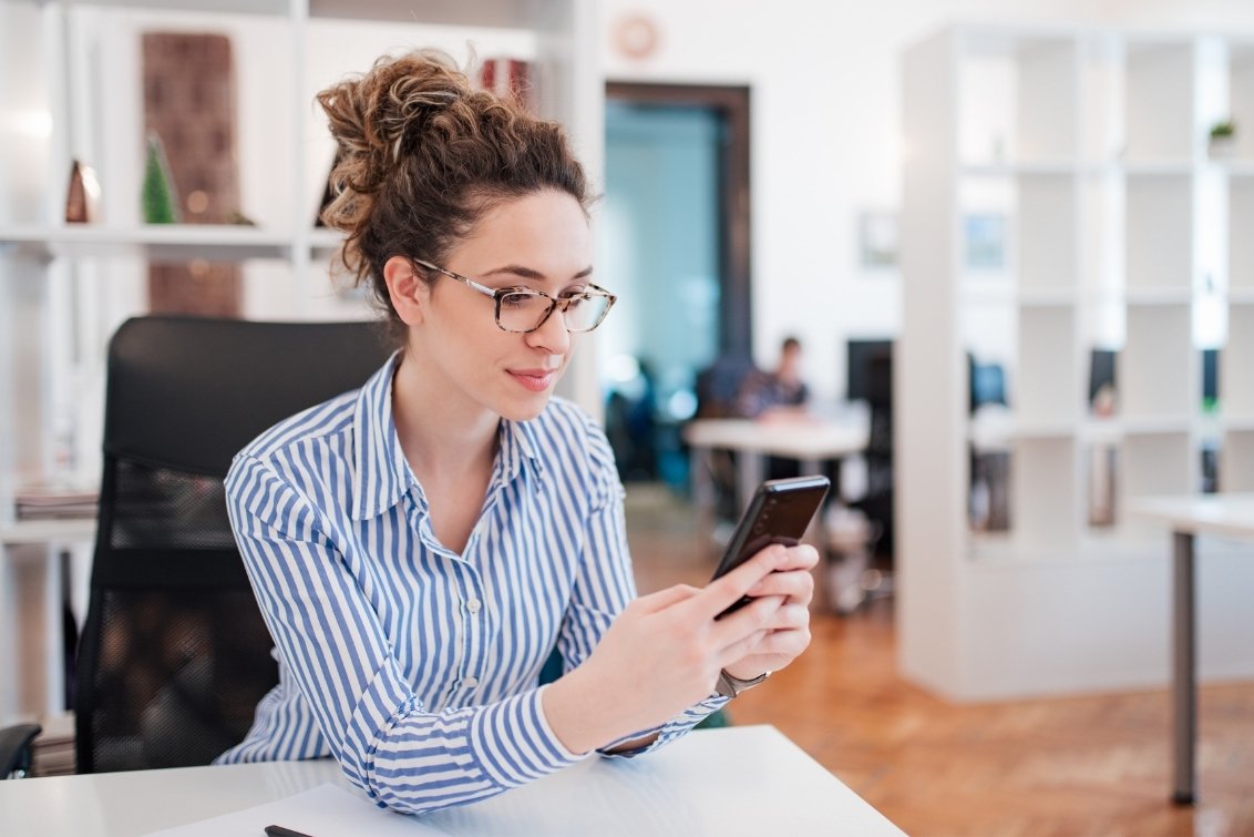 Woman in office environment using smartphone at desk.